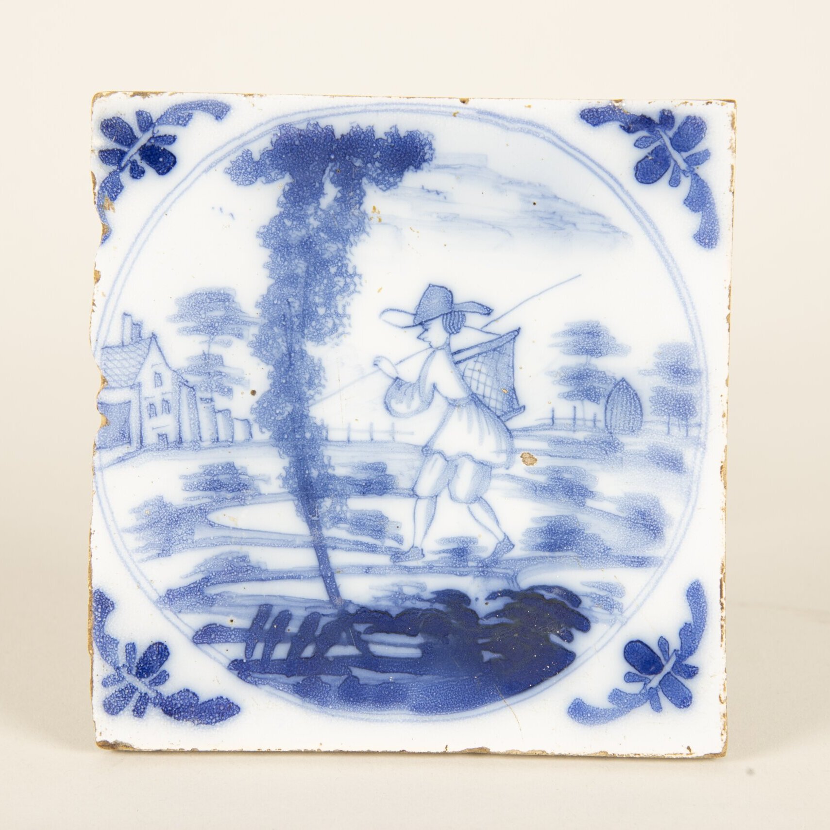 A white and blue tile with a man carrying a basket on his back.