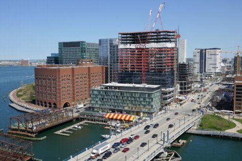 A bridge going across a narrow channel. On the far side of the bridge are many high rises in various stages of construction.