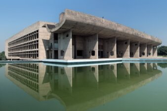 A concrete modern building with a covered deck next to a reflecting pool.