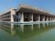 A concrete modern building with a covered deck next to a reflecting pool.