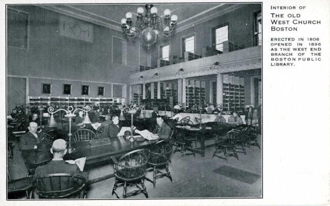 A black and white postcard showing a reading room in a library. There is a balcony above.