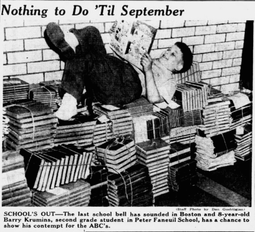 A boy reading a comic book while lying on a pile of books tied with twine.