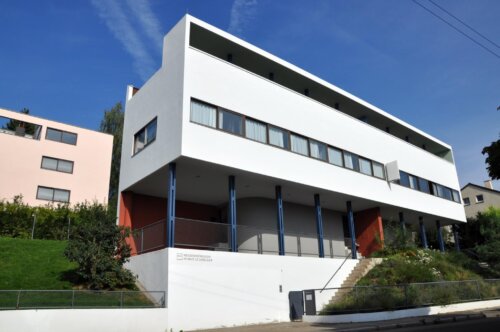 A white modern-style building with long horizontal windows and a facade held up by pillars.