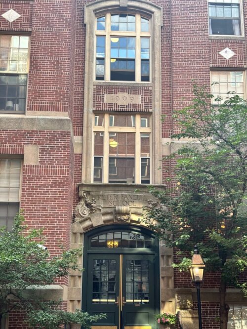 A brick school building with beige trim and solid green doors.