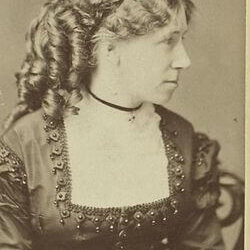 A woman with elaborate curls on the back of her head and a dress with a boxy neckline with a lace collar.