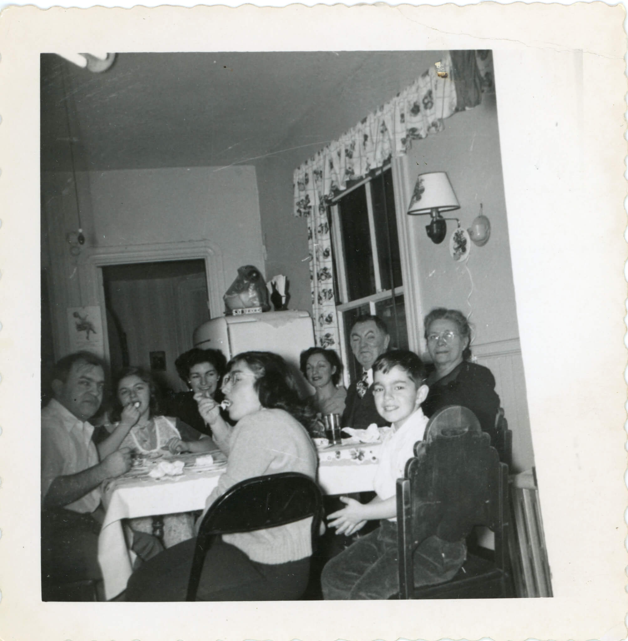 A group of older adults and children sitting around a crowded table in an apartment.