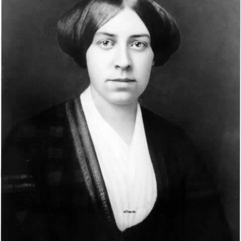 A woman with her hair pulled to the sides of her head covering her ears. She is wearing a wrap style dress with a shirt underneath.
