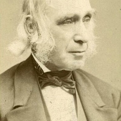 A sepia photo of an older man in a suit with the top of his head bald and large mutton chops.