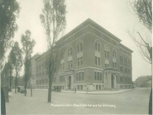 A black and white image of a four story brick building seen from a street corner.