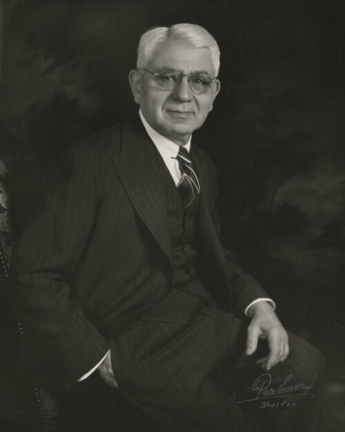 An older man in a suit posing, seated, for a portrait.