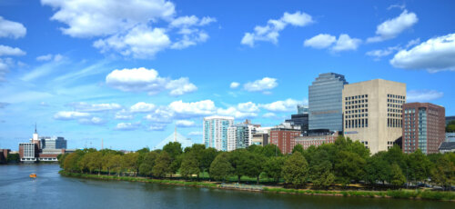 A river scape with several tall buildings over a green embankment.