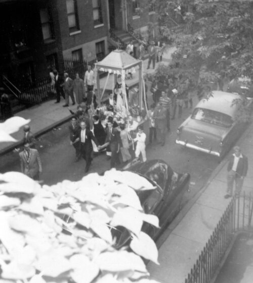 A view from above of a parade being led by a saint being carried in a covered litter.