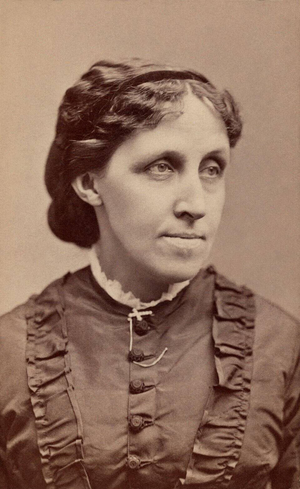 A sepia colored image of a woman with her hair in an up-do with a strong chin and a high collar dress.