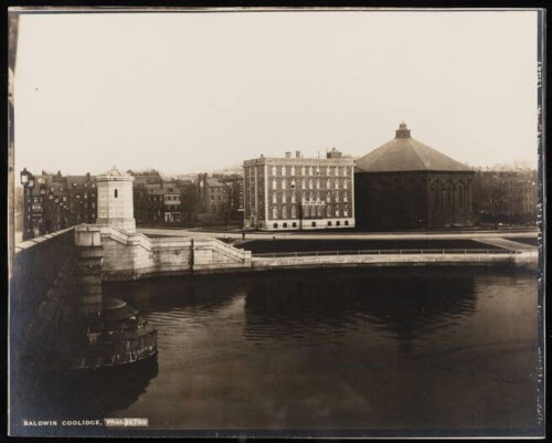 A photo taken from a bridge showing the end of the bridge, a 6 story building and a large hexagonal building.