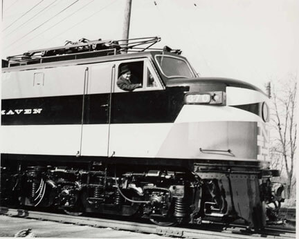 A man hanging out of a window of a large diesal train.