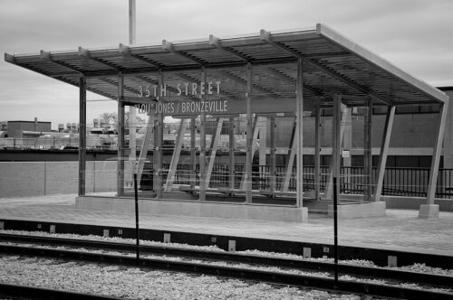 A black and white image of a covered train station with two tracks and a warming area.