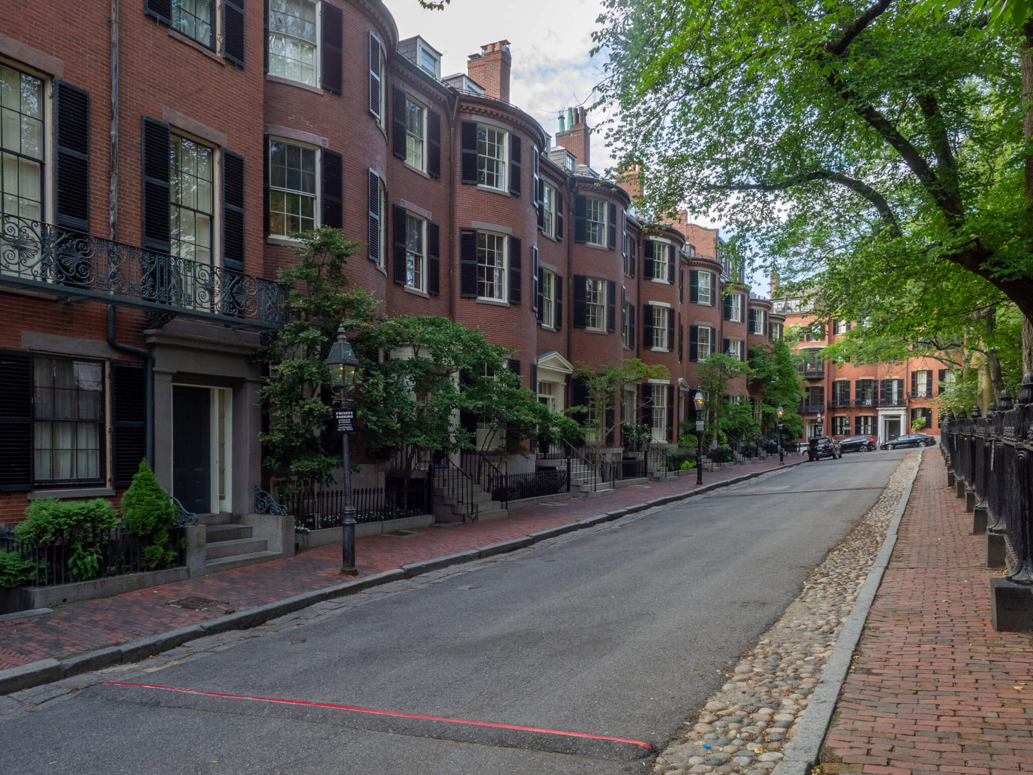 A row of brick townhouses on one side of the street and a fenced in park on the other side.