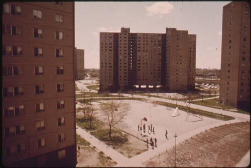 A sepia colored image of several high rise buildings surrounding a courtyard with basketball hoops and playground equitment.