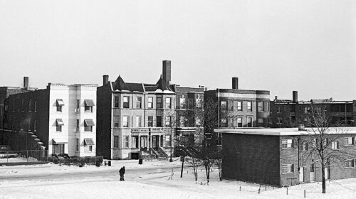 A section of a neighborhood with a mix of project housing and older victorian apartments under a blanket of snow.